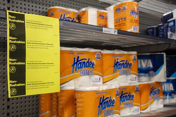 Yellow information poster on shelving with packaged paper towel.