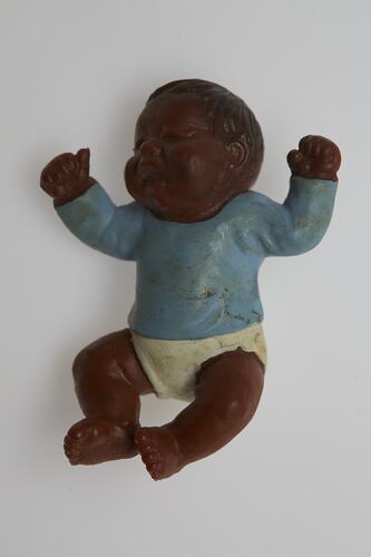 Baby doll wearing a blue top and white pants. The doll has dark brown skin and hair.