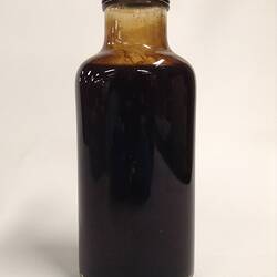 Back of dark glass jar containing crude oil sample.
