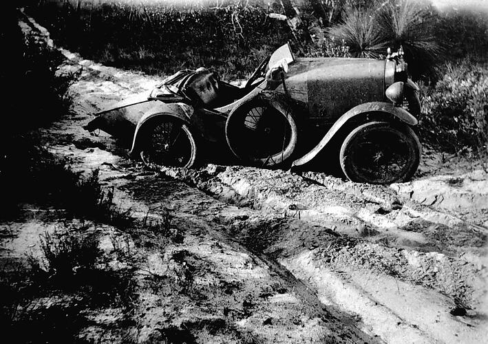 [A home-built baby Austin kit car, bogged in heavy mud, 1930s.]