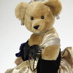 Light brown plush bear in black velvet and gold lame gown. Faux diamond, amethyst tiara, necklace, earrings.