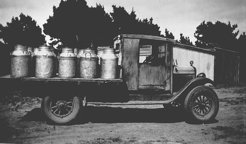 [An early model tray truck loaded with milk cans, Cobden, about 1930. Travelling at speeds of about 25 miles per hour (40 km/h), motor trucks far surpassed the capacity of horses as transport and delivery vehicles.]