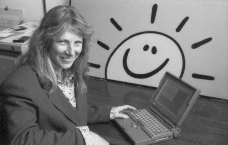 Black and white image of a woman sitting at a desk with a laptop.