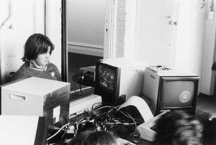 A student surrounded by computer monitors and wires.