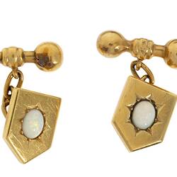 Gold shield shaped cufflinks with central white opals in starcut setting. Chains to barbell togggles.