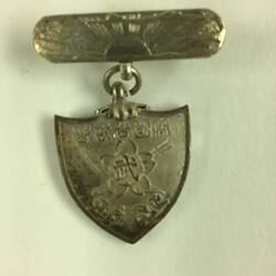 Decorative shield shaped medal suspended from bar pin.