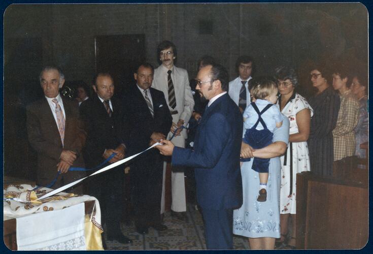 Group watching on as man holds ribbon attached to a stole on a table as part of religious ceremony.