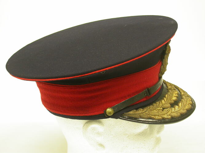 Blue cap with red hat band and leather visor embroidered in gold, side view.