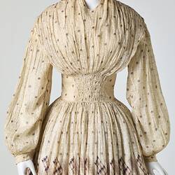 Cream muslin dress, high neck, long sleeves, banded waist, full gathered skirt. Torso detail.