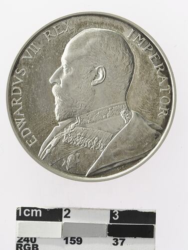 Round silver coloured medal with profile of man and text surrounding,