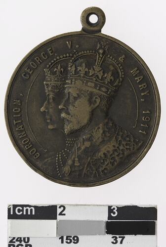 Round bronze coloured medal with profile of crowned man and woman with text surrounding.