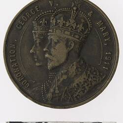 Round bronze coloured medal with profile of crowned man and woman with text surrounding.