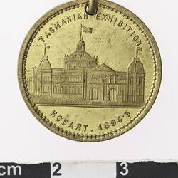 Round gold coloured medal with building and text above and below.