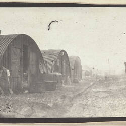 Row of cylindrical corrugated iron huts on left.