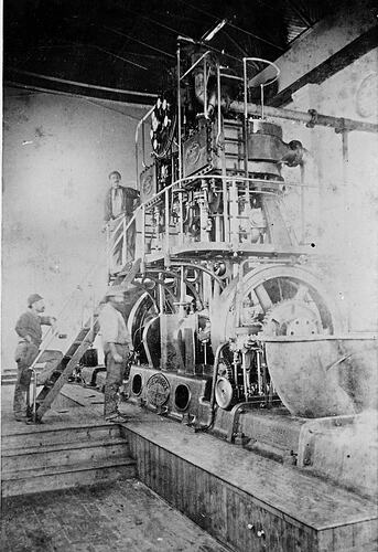 Three men with irrigation pumping engine in engine room.
