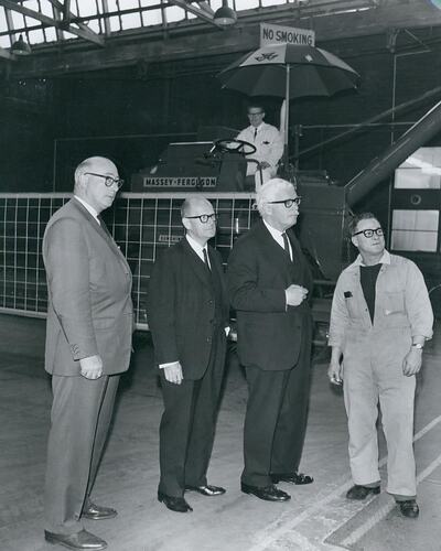 Four men standing in front of an harvester in factory.