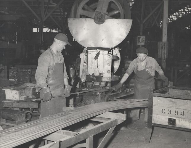 Two men are working a machine cutting steel bars.