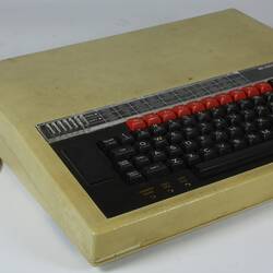 Discoloured, stained beige computer console with black and red keyboard. White cable.
