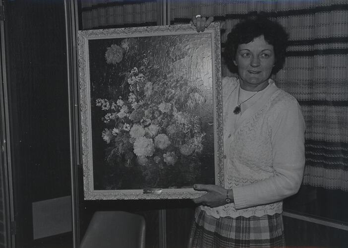 Woman holding framed floral still life.