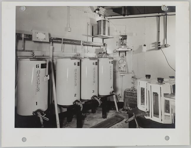 Four vats with hazard warnings, connected to piping.