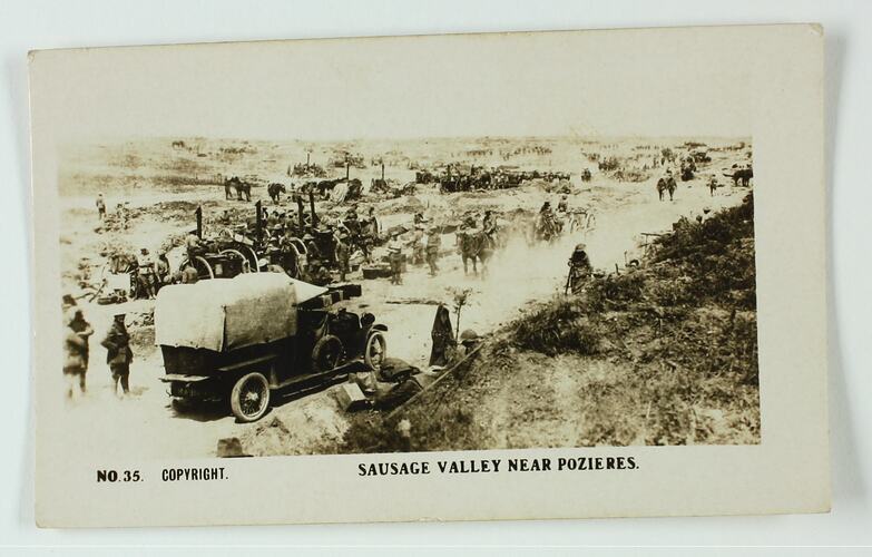Soldiers, horses and a car on a dirt road, the soldiers are setting up artillery.