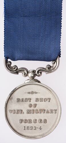 Round silver medal with ornate mount suspended from blue ribbon. Medal has text.
