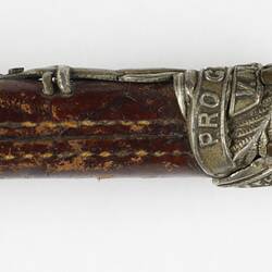 Detail of leather riding crop handle with silver cap and emblem.