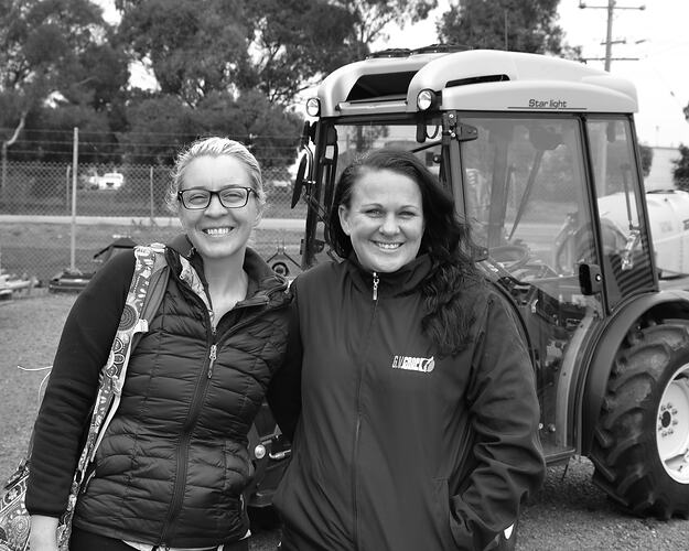 Two women standing next to a tractor.