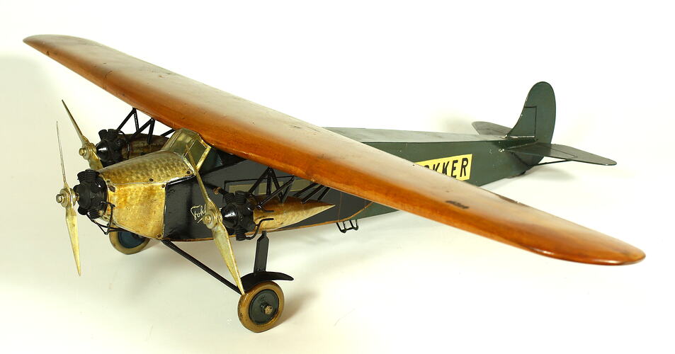 Wooden model aeroplane with green body, natural wood wings and metal front propeller.