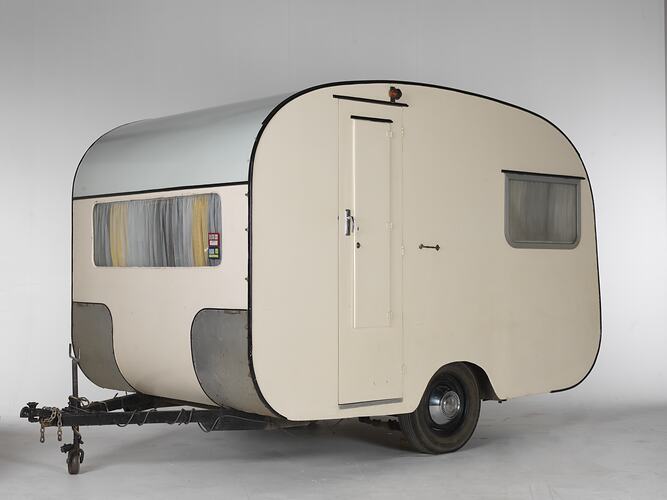 Cream caravan with curved edges and metal trim. Two wheels and tow bar.