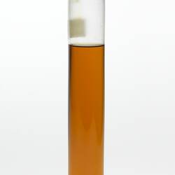 Cylindrical glass jar with amber coloured liquid. One label affixed, sealed at top.