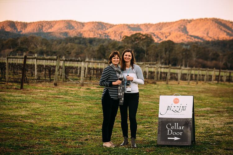 Two women in vineyard, next to sign.