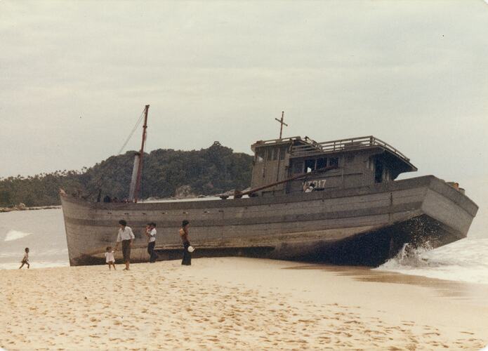 Wooden boat aground at beach with people nearby.
