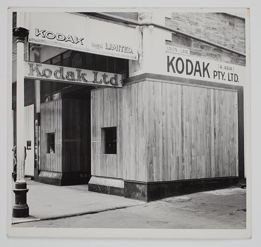 Shopfront with boarded up windows and Kodak sign.