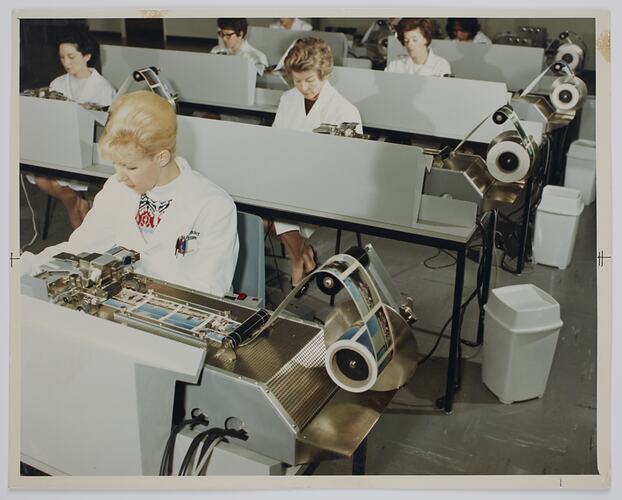 Group of women seated at desks with machines.