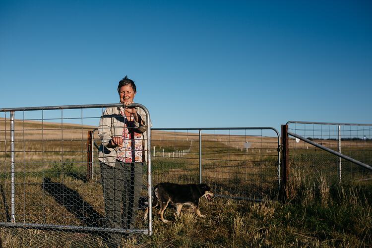 Woman with dog at paddock gate.