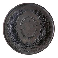 Round medal with wreath around, text within and below.