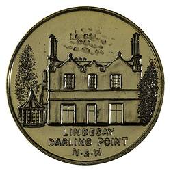 Round medal with two storey house and trees.