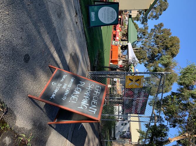 Market scene with chalkboard sign in foreground. Stalls and trees behind.