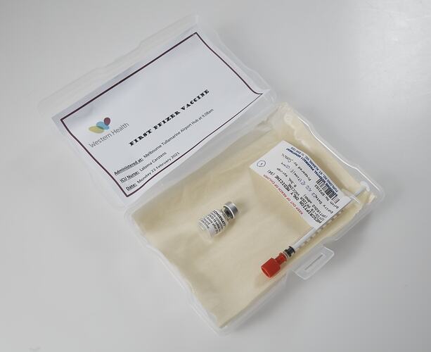 Labelled syringe and vial in lined plastic box on angle. Card in lid has printed text. White background.