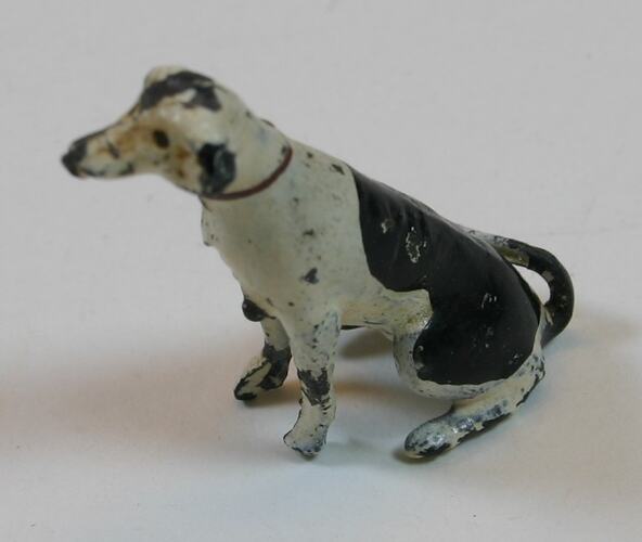 Toy metal sitting dog painted black and white. Paint is chipped and worn.