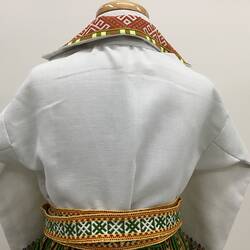 Back of cream shirt with long sleeves. Colourful embroidered edging at collar and around waist.