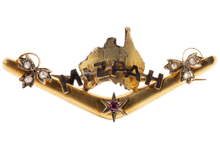 Gold boomerang with a map of Australia behind the words 'Mizpah'. Has seed pearls and a small ruby.