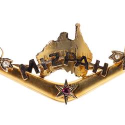 Gold boomerang with a map of Australia behind the words 'Mizpah'. Has seed pearls and a small ruby.