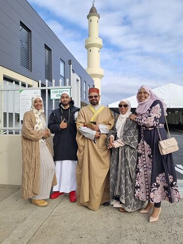 Three women and two men pose in front of a mosque.