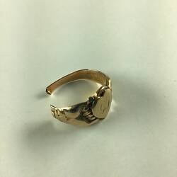 Broken women's gold ring with two clasped hands around a central love heart, inscribed with the worn cursive letters GS.