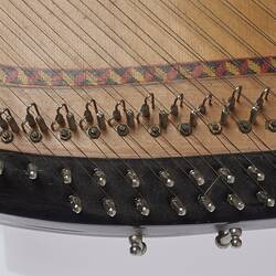 Detail of the base of a timber stringed instrument. Pale wood with black laquered timber detail. Multi stringed.