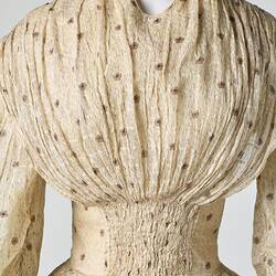 Cream muslin dress, high neck, long sleeves, banded waist, full gathered skirt. Bust detail.