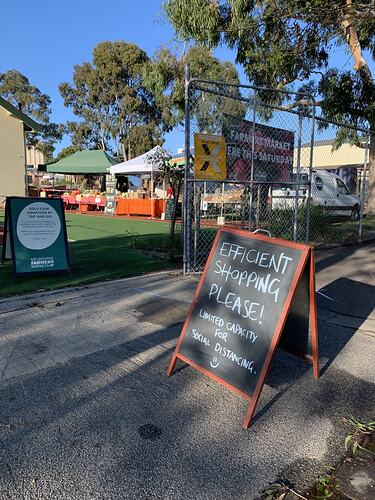 Market scene with chalkboard sign in foreground. Stalls and trees behind.