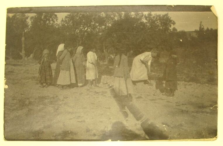Girls watching a woman in white playing croquet.